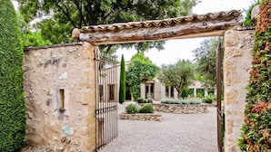 Un portón de piedra rústica con una cerca de metal, que da a un patio de grava con una pérgola.