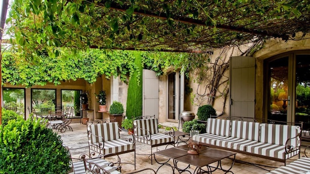 Un patio al aire libre con mobiliario a rayas, una mesa y una pared verde cubierta de follaje.