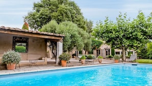 Un área de piscina con pérgola, asientos y plantas en macetas.