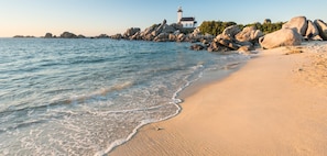 Una playa con un faro, rocas grandes y aguas tranquilas.
