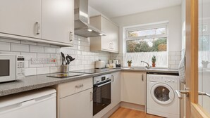 A modern kitchen with white cabinets, a built-in oven, a microwave, and a washing machine.
