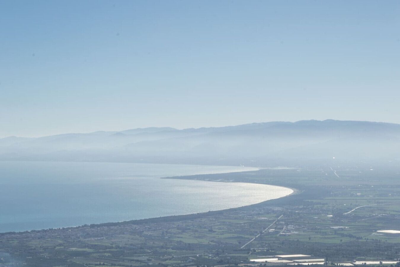 A coastal landscape with a curved shoreline, distant mountains, and a town in the foreground.