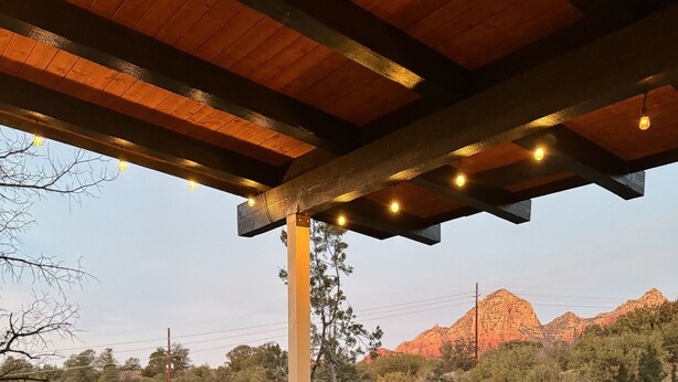 Terraza exterior con un brasero, mobiliario de madera y vistas a formaciones rocosas rojas.