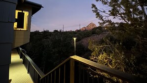 Una escalera lleva a un balcón con vistas a una montaña y árboles bajo un cielo nocturno.