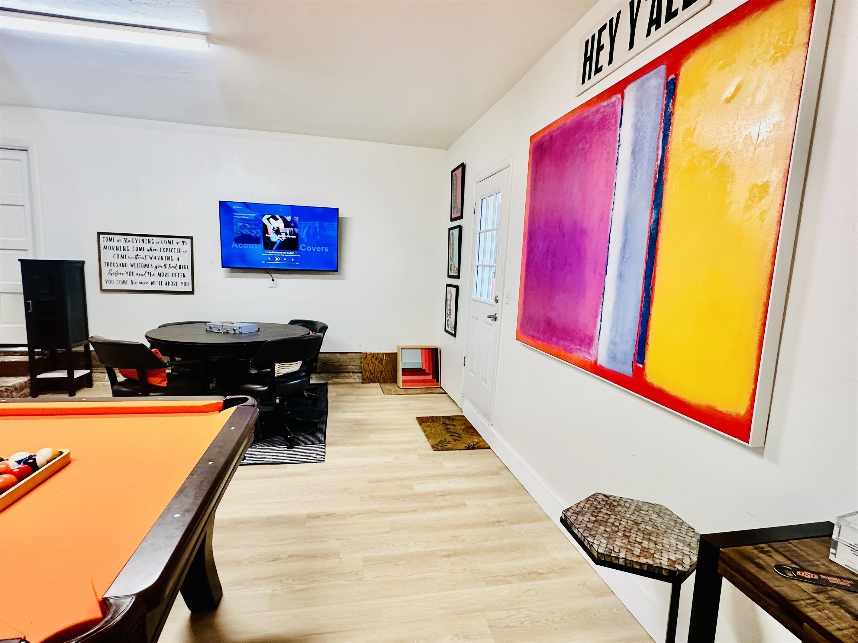 A room with a pool table, a television, and a large abstract painting on the wall.