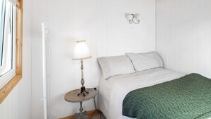 Une chambre avec un plafond en bois, une table ronde avec une lampe, un lit recouvert d’une couverture verte et un luminaire fixé au mur.