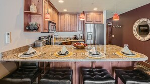 Una cocina con armarios de madera, un refrigerador de acero inoxidable e una isla central con taburetes de bar.