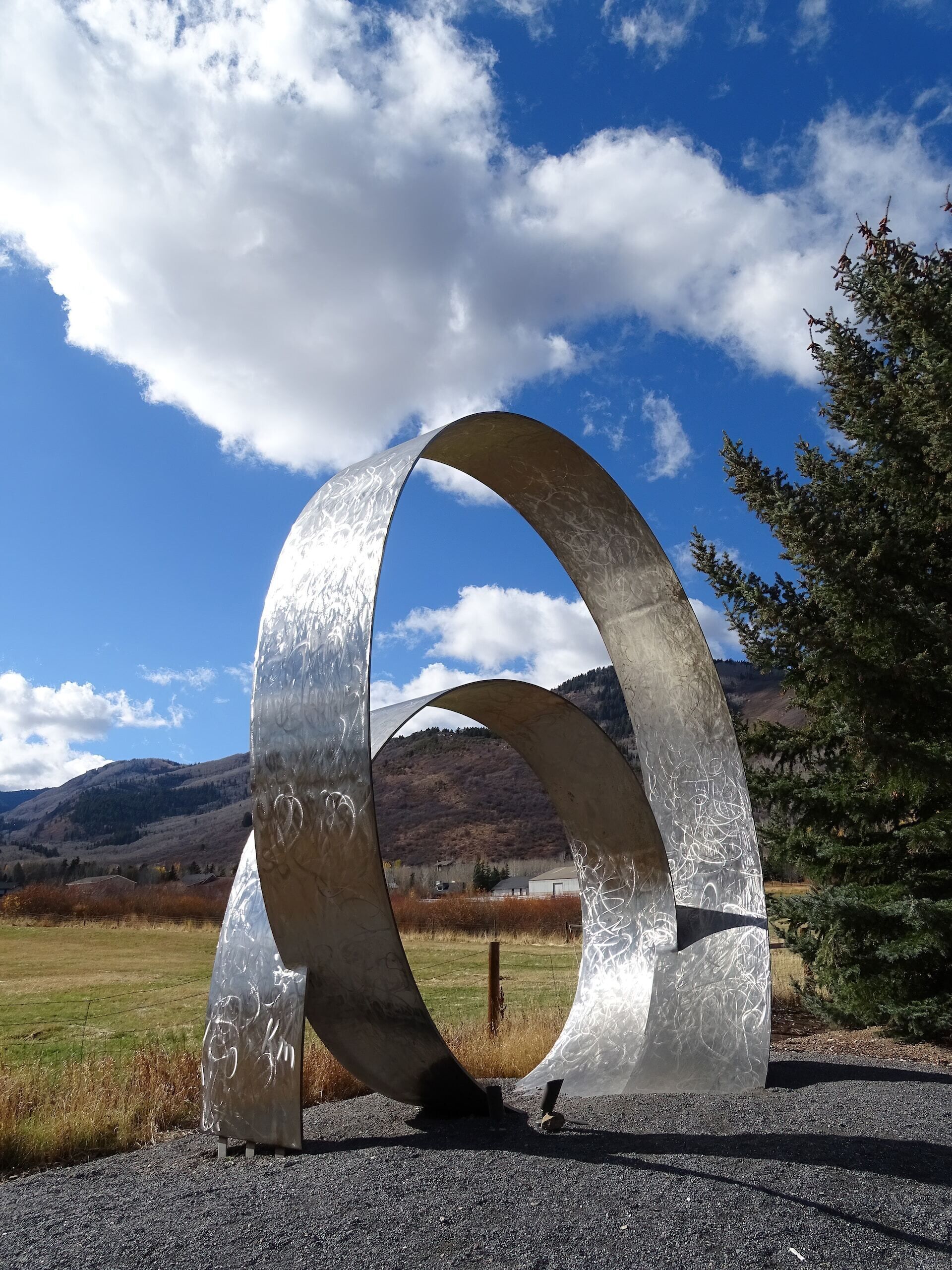 A large metallic sculpture in an open field with mountains in the background.