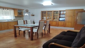 A dining area with a wooden table and chairs, a sofa, and a kitchen with wooden cabinets and a tiled backsplash. - Casa Rural Muito Tranquila (Ortigosa de Cima)