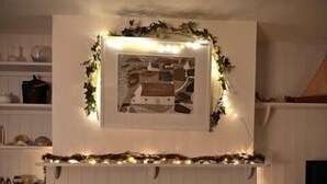 Ett mysigt rum med en öppen spis, en inramad tavla ovanför och en hink med texten ”CANDLEWOOD” på.