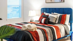 A neatly made bed with a blue headboard, a striped blanket, and several pillows in red, black, and white.
