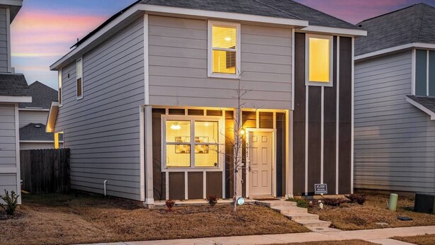 A two-story residential building with a front entrance, a visible garage door, and a well-maintained lawn.