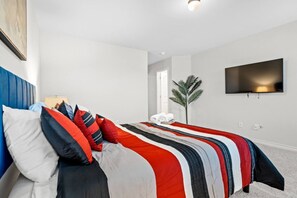 Relax in a serene space with a neatly made bed, flat-screen TV, and a touch of greenery.
