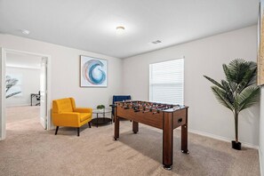 Relax in this stylish room featuring a foosball table, two comfortable armchairs, and a vibrant abstract art piece.