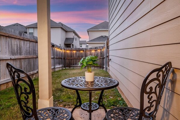 Enjoy a peaceful outdoor retreat with a round table and two chairs, surrounded by lush greenery and a charming wooden fence.
