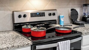 A kitchen with a stainless steel stove, two red pots, a waffle maker, and a can of soda.