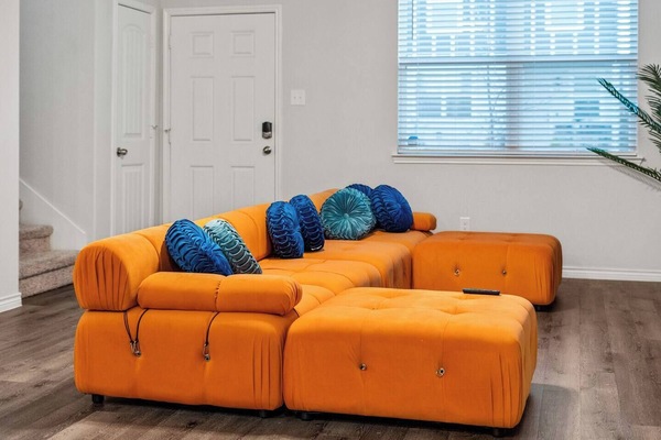 Vibrant living area with a bold orange sectional sofa, perfect for relaxing or watching TV. The plush cushions add a pop of color and comfort to the space. Ideal for family gatherings or unwinding after a day of exploring. Cozy, inviting atmosphere.
