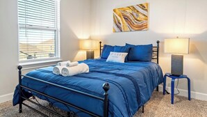 Une chambre à coucher avec un lit, deux lampes de chevet, une fenêtre avec des stores et un tableau abstrait accroché au mur.