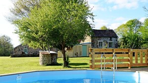 Une piscine avec une terrasse en bois et un bâtiment en pierre en arrière-plan.