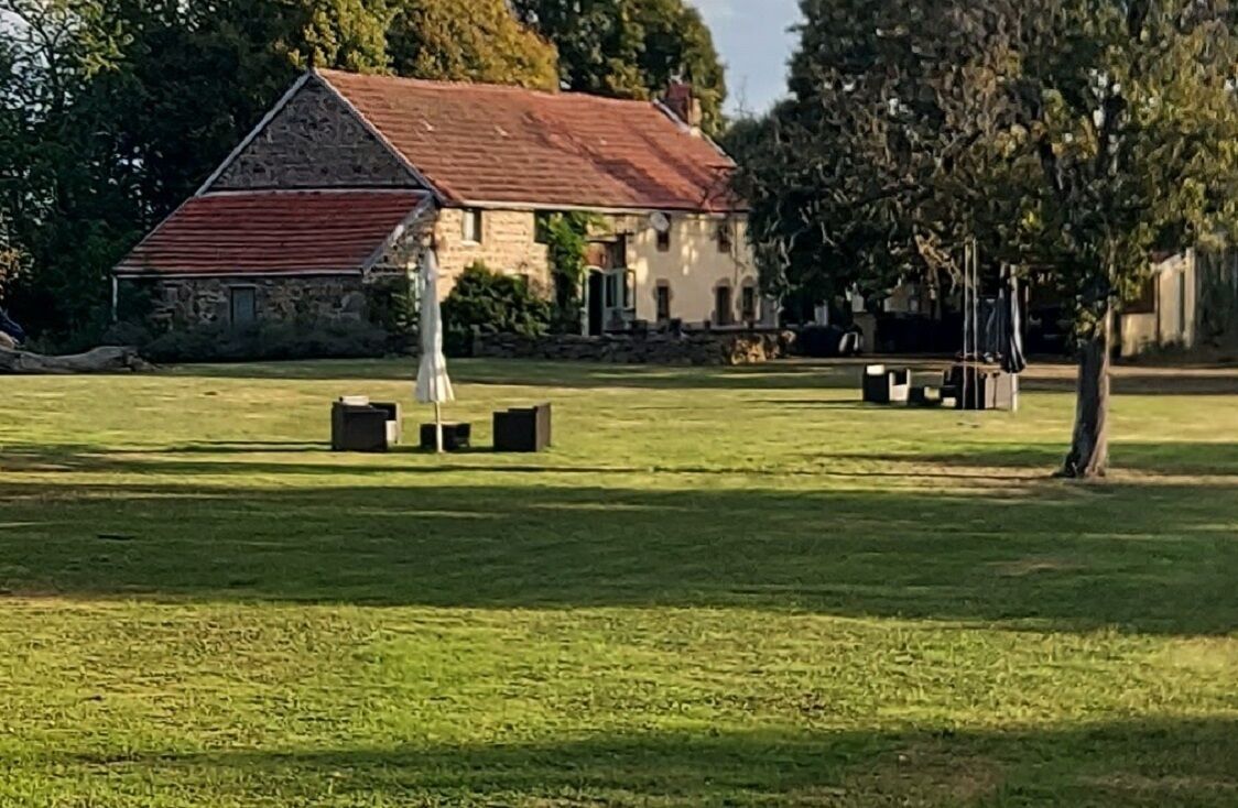 Een grasveld met een stenen gebouw, voorzien van een rood dak en een witte omheining.