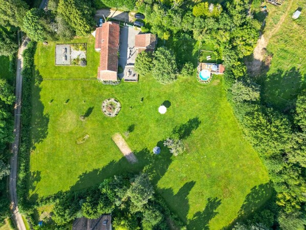 Vista aérea de una propiedad residencial con un amplio jardín, piscina y garaje independiente.