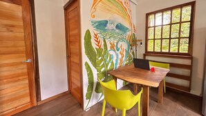A room with a wooden door, a mural with marine life, a wooden table with a laptop, a yellow chair, and a window with a view of greenery. - Villa Ocean Coral Luxury Beachfront Villa just steps away from the beach! (Punta Uva)