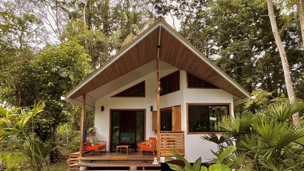 A two-story wooden cabin with a balcony, surrounded by lush greenery. - Villa Ocean Coral Luxury Beachfront Villa just steps away from the beach! (Punta Uva)