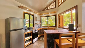 A compact kitchen with a refrigerator, stove, sink, and wooden dining table. - Villa Ocean Coral Luxury Beachfront Villa just steps away from the beach! (Punta Uva)