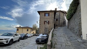 Un edificio de piedra con techo de tejas, coches aparcados y una calle empedrada.