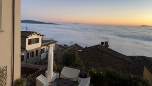 Una terraza con asientos al aire libre, con vistas a un pueblo y un mar de nubes.