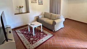 Una sala de estar con un sofá, una mesita, un televisor, un tapete rojo y un techo con vigas a la vista.