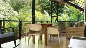 Un espace extérieur abrité, aménagé avec une table et des chaises, et entouré d’une végétation luxuriante.