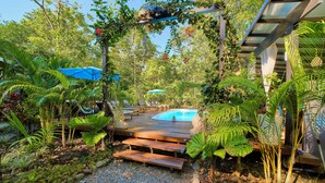 Un espace piscine agrémenté d’un escalier en bois menant à la piscine, entouré d’une végétation luxuriante et surmonté d’une pergola couverte de plantes grimpantes.