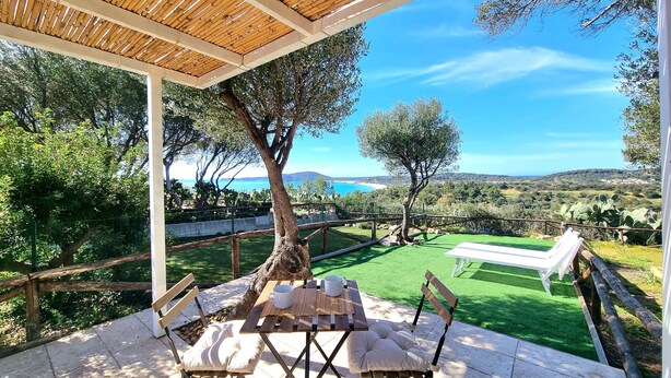 An outdoor patio with a wooden table and chairs, a pergola, and a view of the sea and hills. - Moon House 350mt from the beach Sea view Garden Free private parking  (Villasimius)