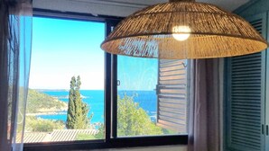 A room with a large window offering a view of the sea and greenery. - Moon House 350mt from the beach Sea view Garden Free private parking  (Villasimius)