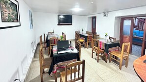 Un comedor con varias mesas y sillas, un televisor montado en la pared y una puerta que da a un balcón.