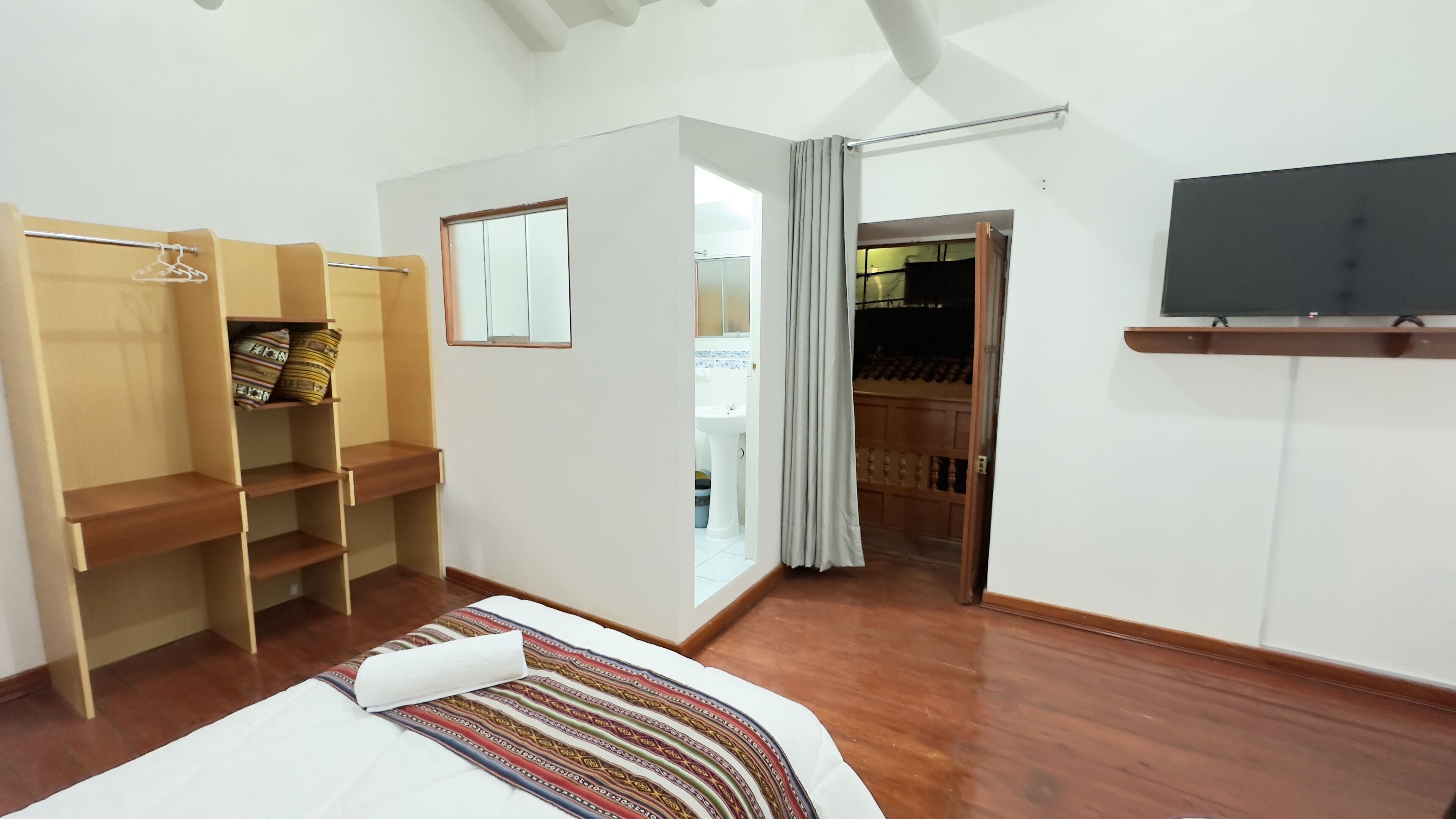 Une chambre à coucher comprenant un lit, une armoire, un téléviseur et une salle de bain visible à travers une porte ouverte.
