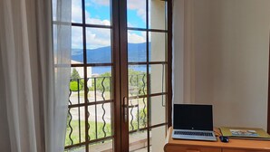 Ein Zimmer mit großem Fenster, einem Laptop auf einem Tisch und einem Buch.