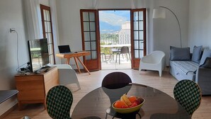 Ein modernes Wohnzimmer mit Esstisch, Stühlen, einer Couch und einem Laptop auf einem Schreibtisch.