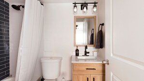 Ein Badezimmer mit Toilette, Holzschrank, Spiegel und Duschvorhang.