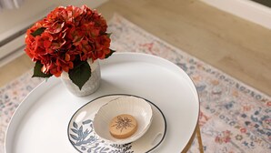 Ein weißes Tablett mit einer dekorativen Schale und einem Blumenstrauß auf einer gemusterten Tischdecke.