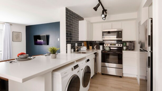 Eine moderne Küche mit integrierter Waschmaschine und Trockner, Edelstahlgeräten und einem flachbildschirmfernseher an der Wand.