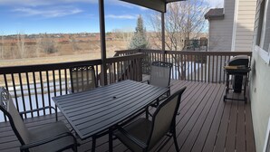A wooden deck with a table and chairs, a grill, and a view of a snowy landscape.