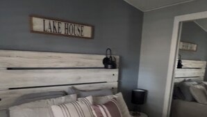 Un dormitorio con cama, almohadas, cabecera, ventilador de techo, mesita de noche y espejo.