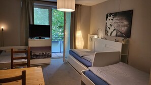 A hotel room with a bed, a desk, a chair, a television, and a window with a view of greenery. - Budget & Central 3Room Apt+Balcony & WiFi (Hamburg)