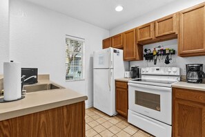A kitchen with wooden cabinets, a white refrigerator, a stove, and a coffee maker. - Beautiful Florida Condo  (Kissimmee)
