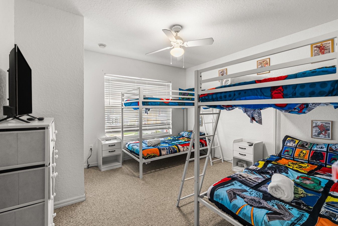 A bunk bed room with a ceiling fan, a desk, and a window with blinds.