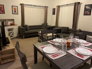 Un coin repas avec une table dressée pour quatre personnes, un canapé et un téléviseur en arrière-plan.