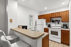 A compact kitchen with wooden cabinets, a white refrigerator, a stove, and a coffee maker. - Beautiful Florida Condo  (Kissimmee)