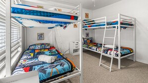 Ein Schlafraum mit Etagenbetten, Deckenventilator, Fenster mit Jalousien und einem kleinen Nachttisch.